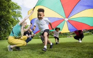 Children playing with a parachute at school during pe in the North East of England. A boy is running underneath it.